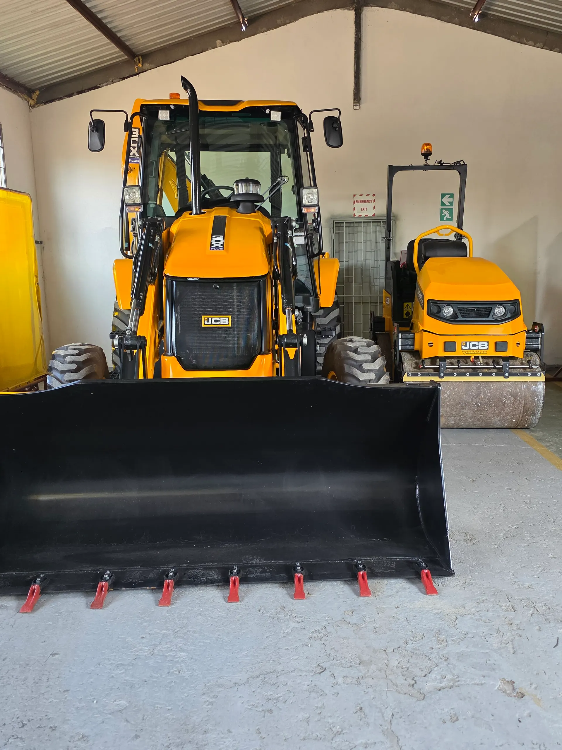 A JCB TLB and a roller parked in the yard