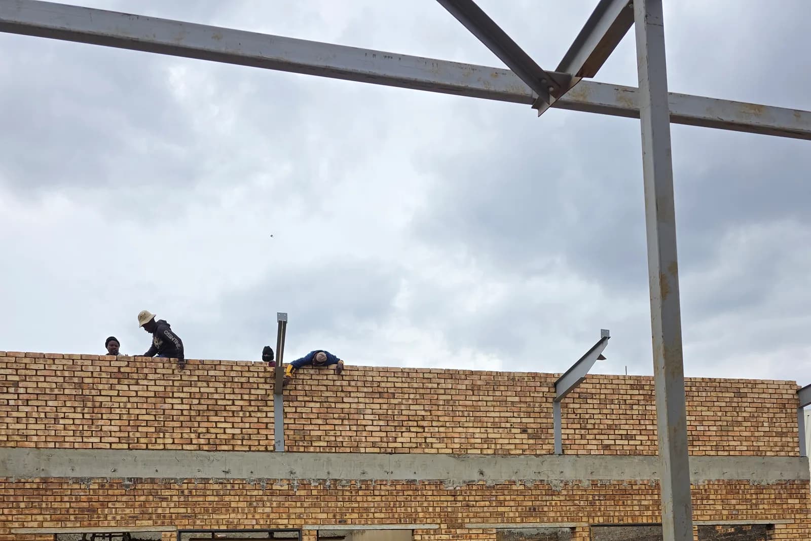 Bricklayers on a new wall under a steel roof frame